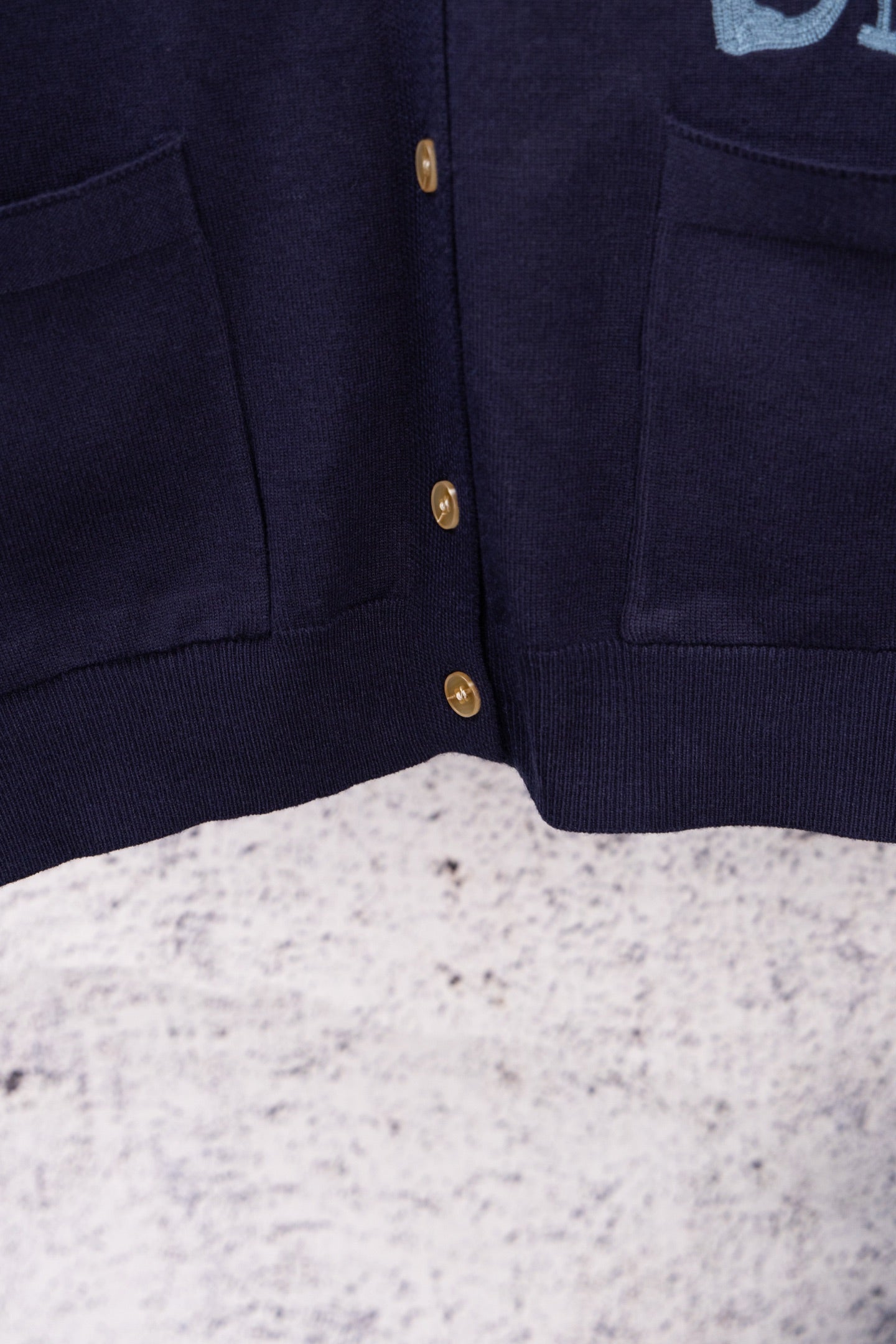 Navy cardigan front placket with gold button row and side pockets