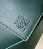 Teal leather bag detail with embossed logo on front panel and stitched edge
