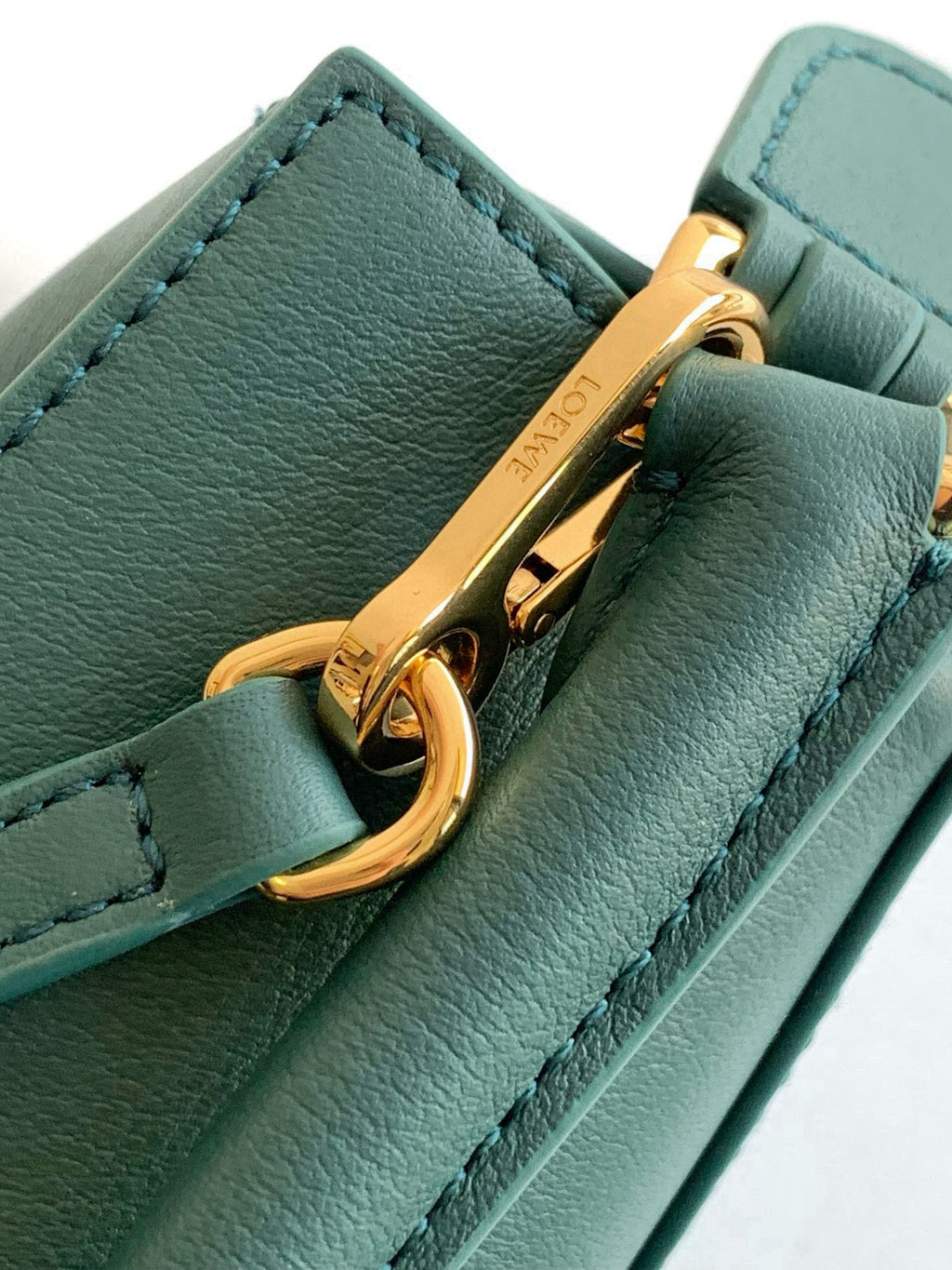 Gold zipper pull on teal Loewe leather bag with stitched edges