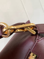 Close-up of gold hardware clasp on burgundy leather bag with stitched trim