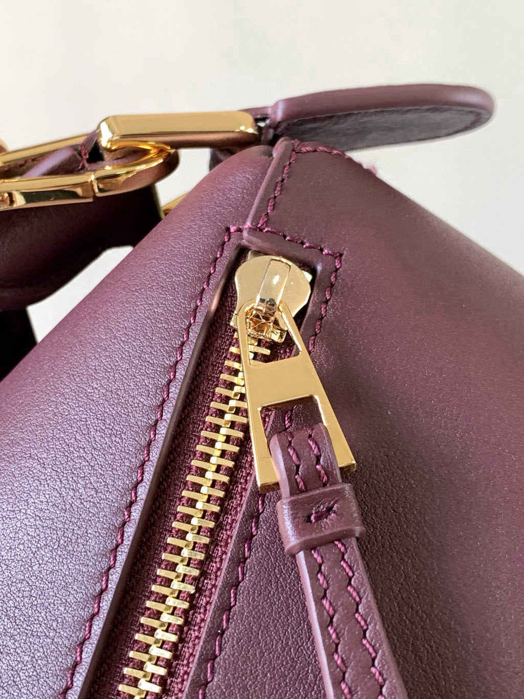 Close-up of burgundy leather zip pull and gold zipper hardware with strap loops