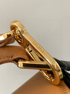 Gold-tone clasp and ring on tan leather bag strap hardware.