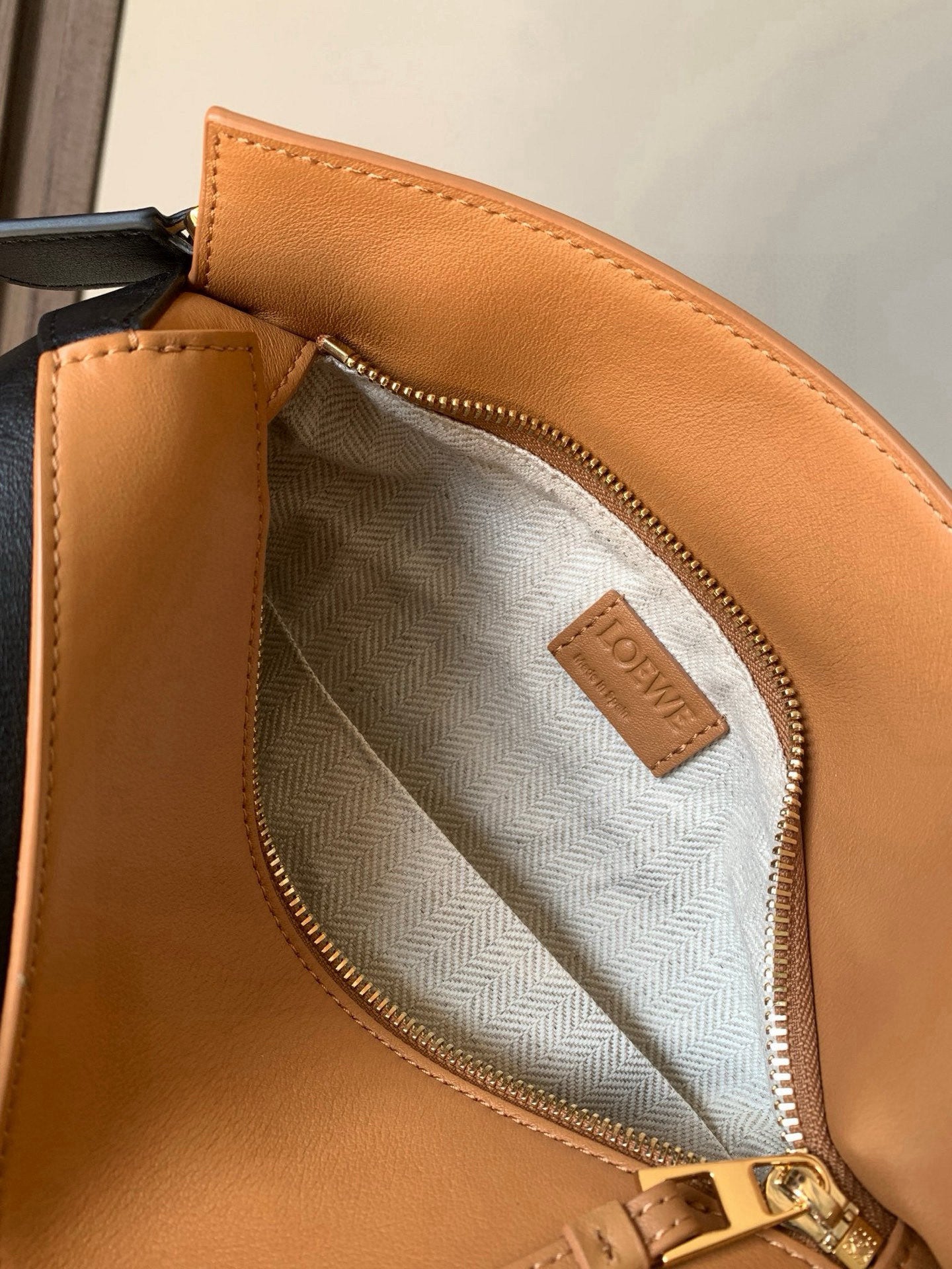 Tan leather bag interior with light gray herringbone lining and stitched logo label.