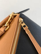 Bag top zipper track and gold pull on tan and black leather with strap.