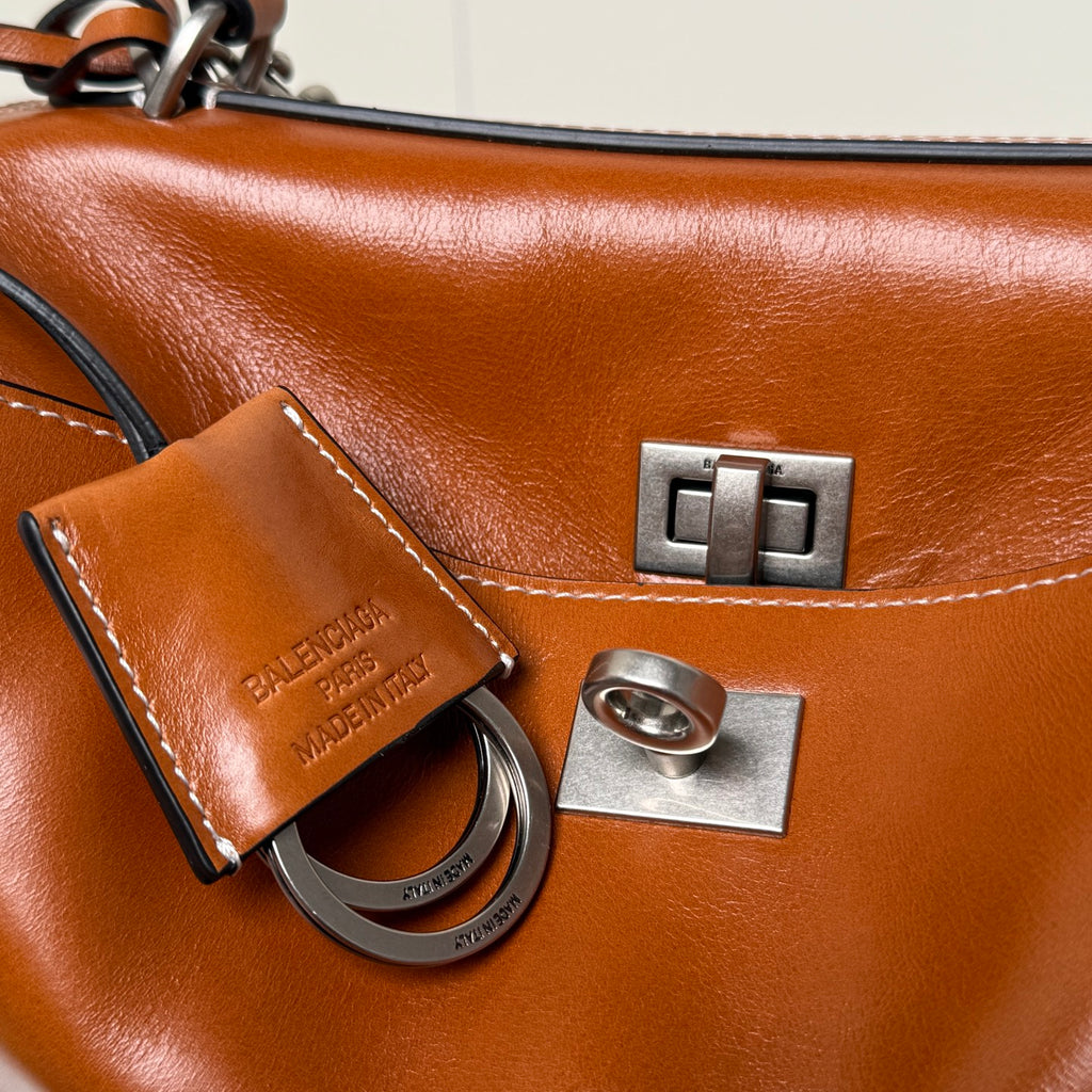 Balenciaga leather bag close-up with metal clasp, stitched strap tag, and engraved logo plate