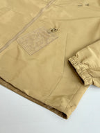 Beige long pants with embossed logo patch on front pocket