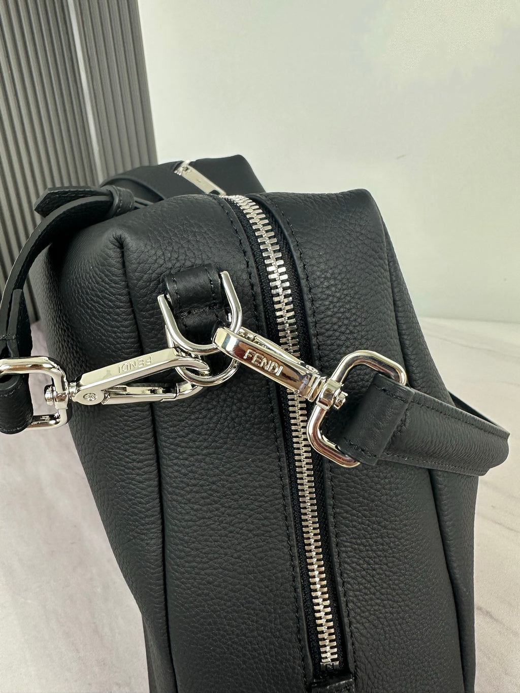 Fendi dark leather bag with front zip pull, metal rings, and crossbody strap