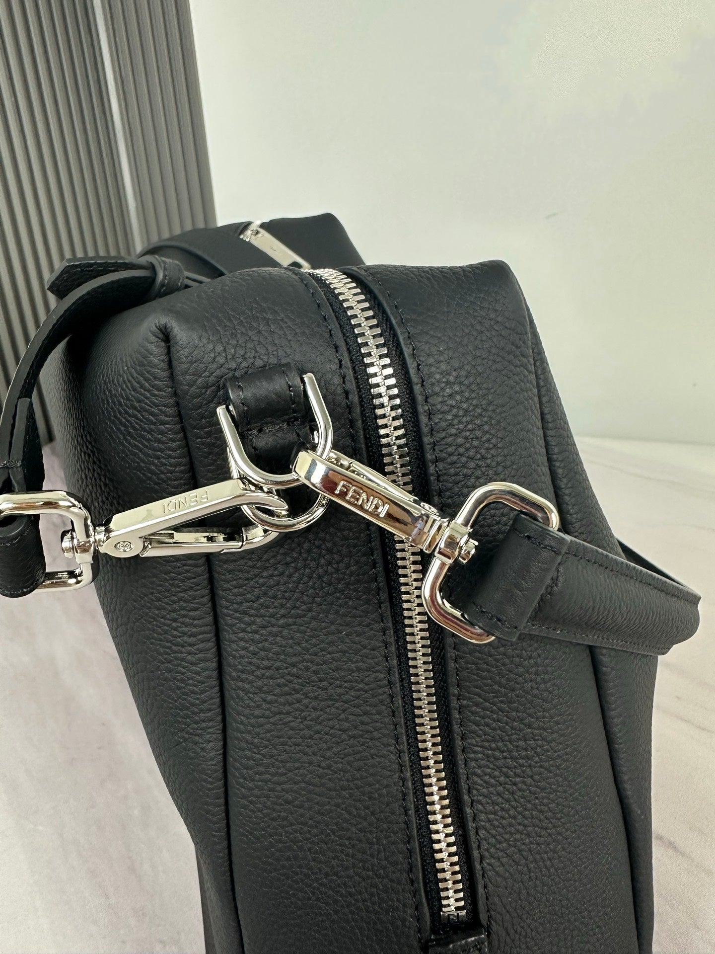 Fendi dark leather bag with front zip pull, metal rings, and crossbody strap