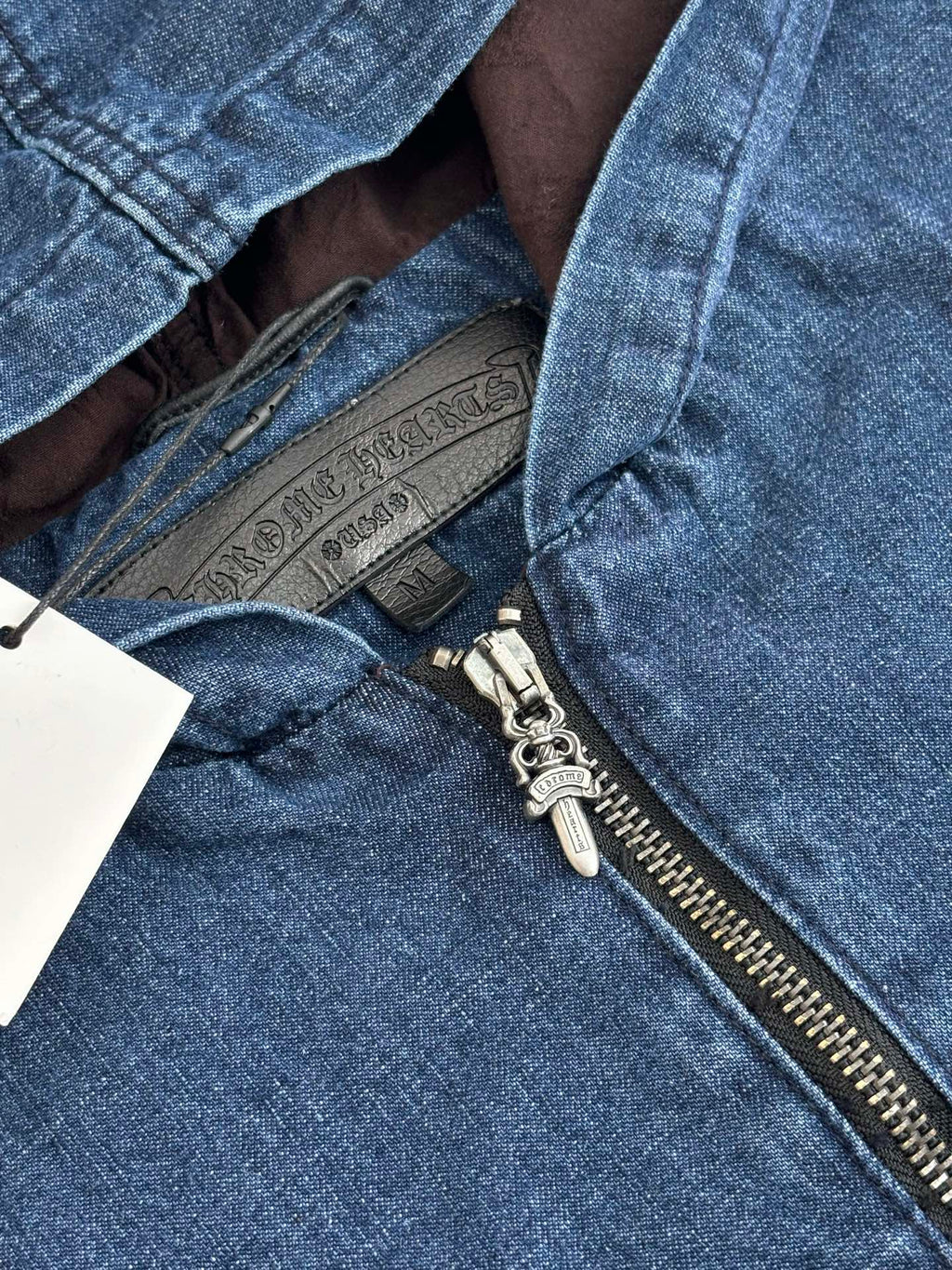 Blue denim jacket detail showing half-zip hardware and inner brown lining at opening.