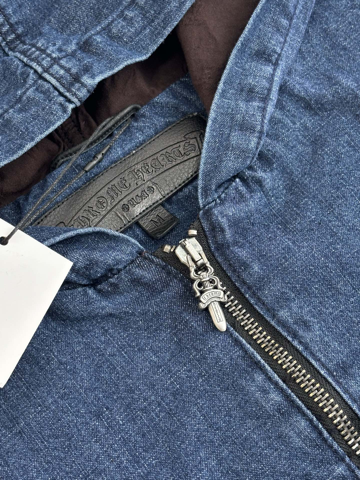 Blue denim jacket detail showing half-zip hardware and inner brown lining at opening.