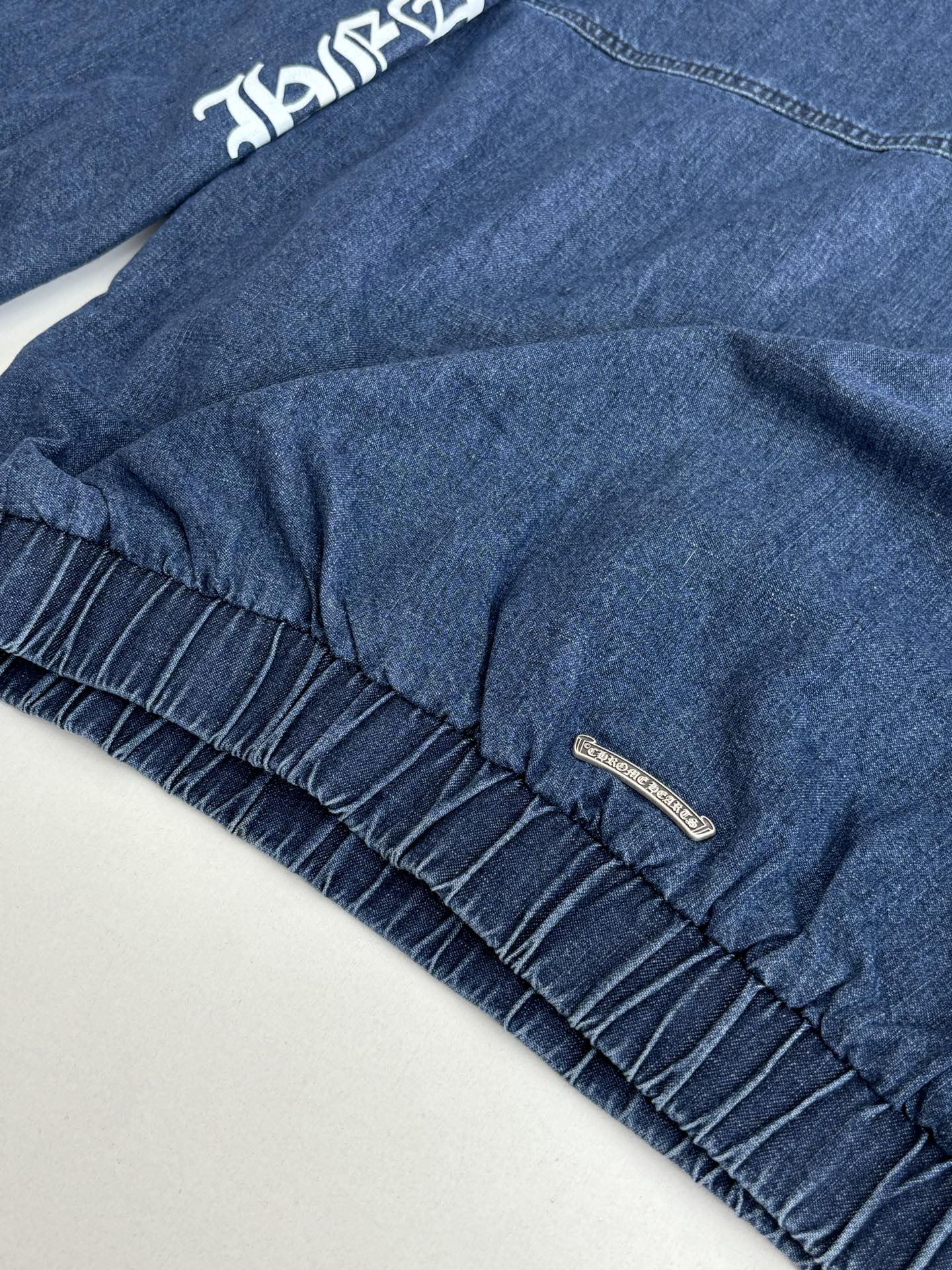 Blue denim jacket hem detail with gathered ruffle trim and small metal brand tag.