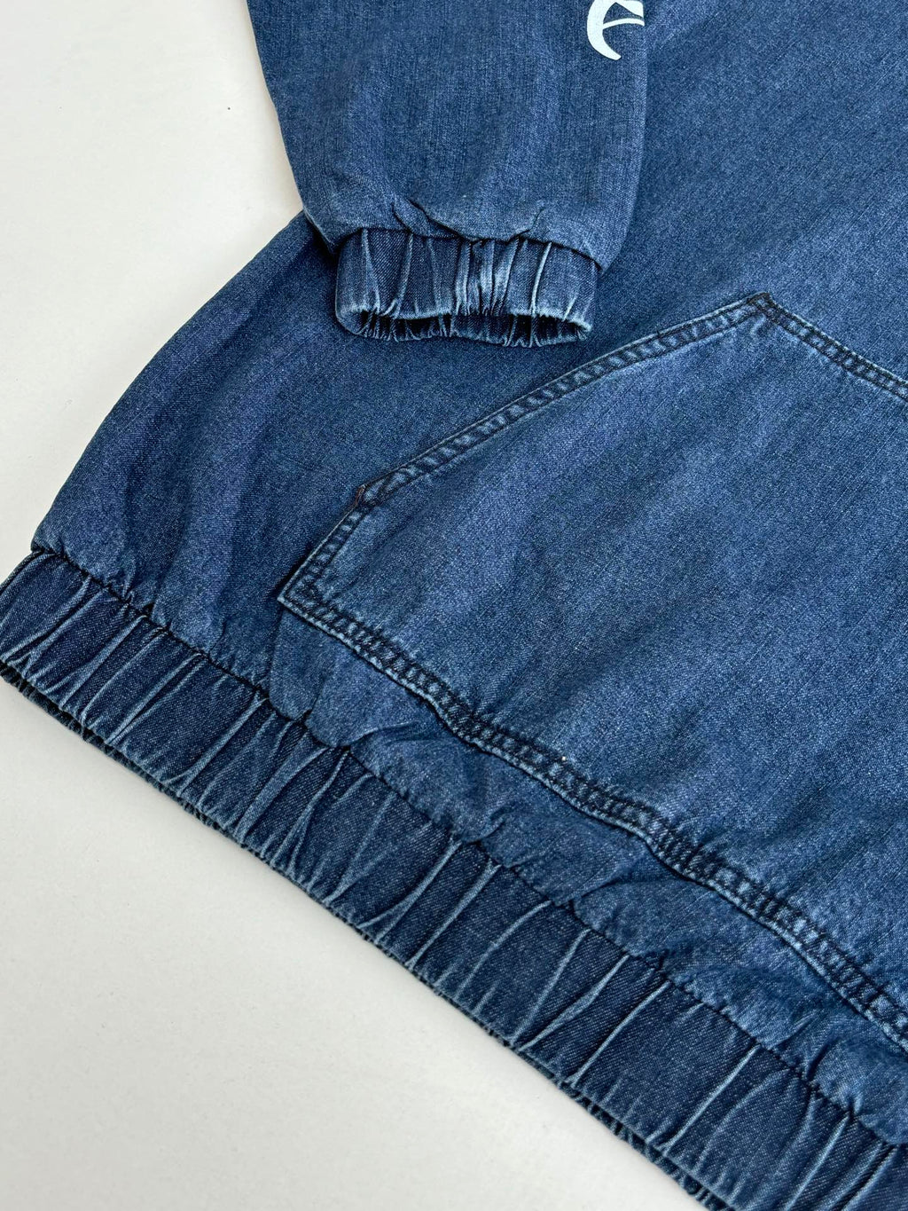 Blue denim hooded jacket with ruffled trim at cuffs and front seam details.