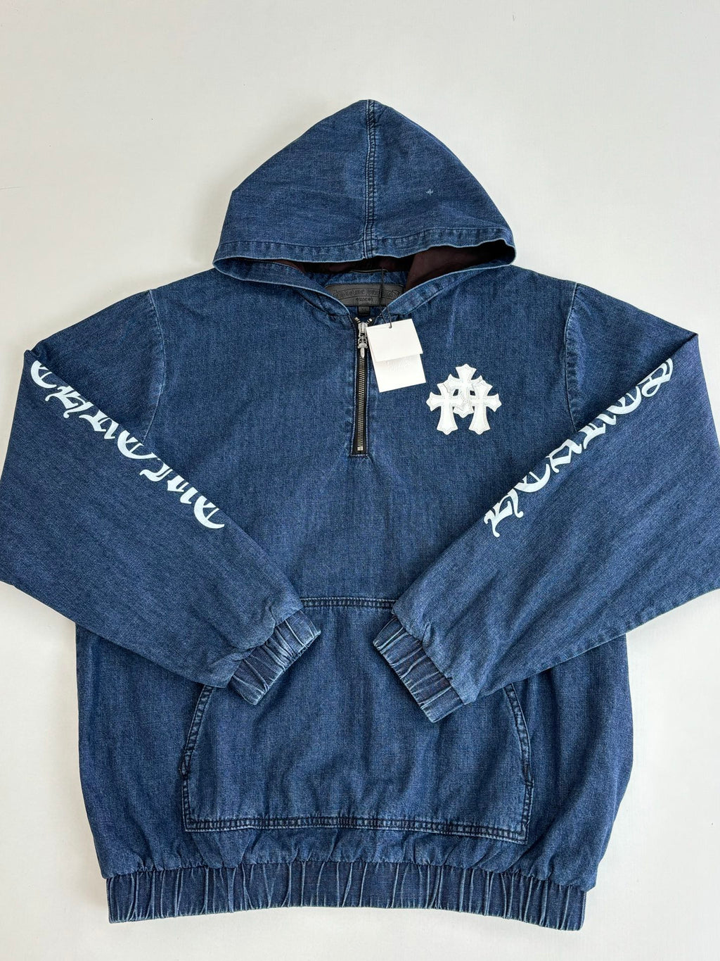 Blue denim hooded jacket with half-zip and white cross emblem; long sleeves with text print.