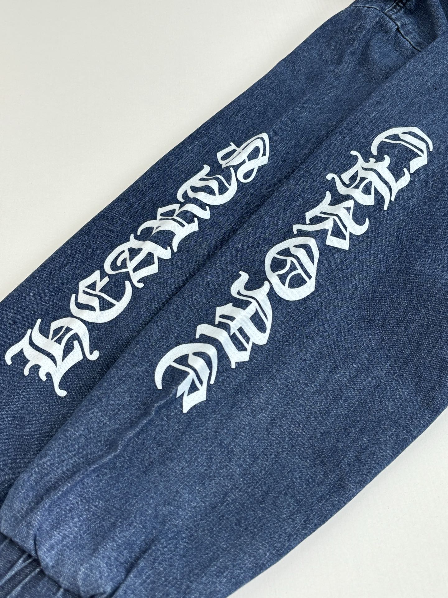 Blue denim long pants with white graphic lettering on one leg