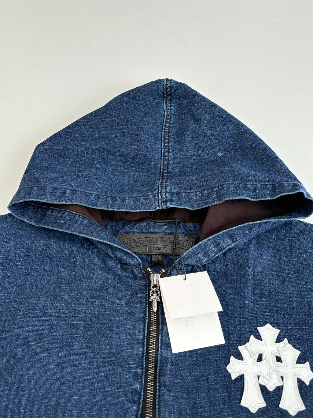 Blue denim hooded jacket with half-zip, white emblem patch, and metal zipper pull.