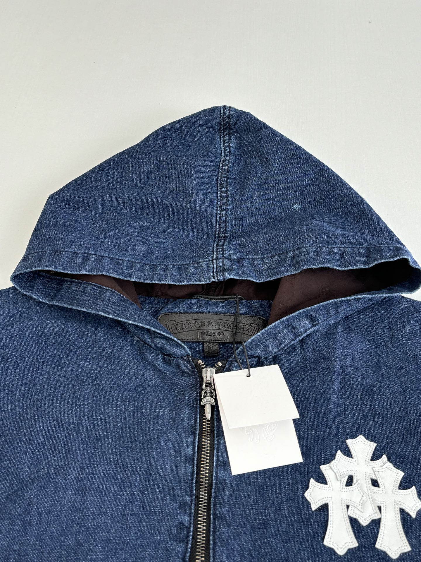 Blue denim hooded jacket with half-zip, white emblem patch, and metal zipper pull.