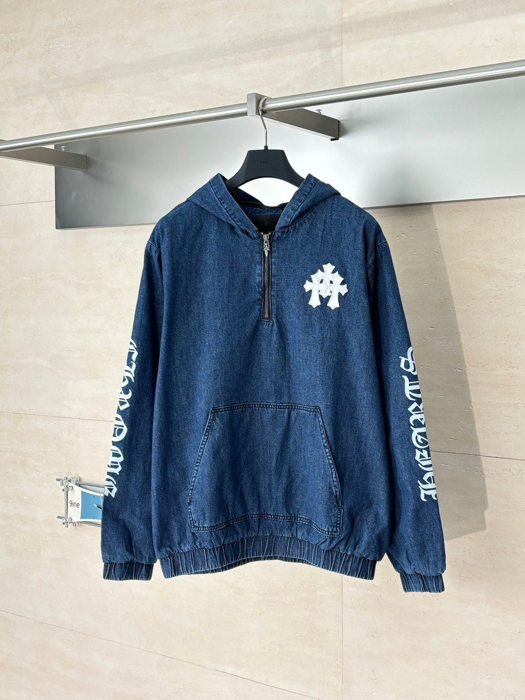 Denim hooded jacket in blue with half-zip front and white embroidered emblem on chest.