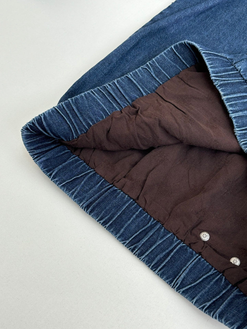Blue denim hooded jacket with gathered ruffle hem and dark inner lining at hood opening.