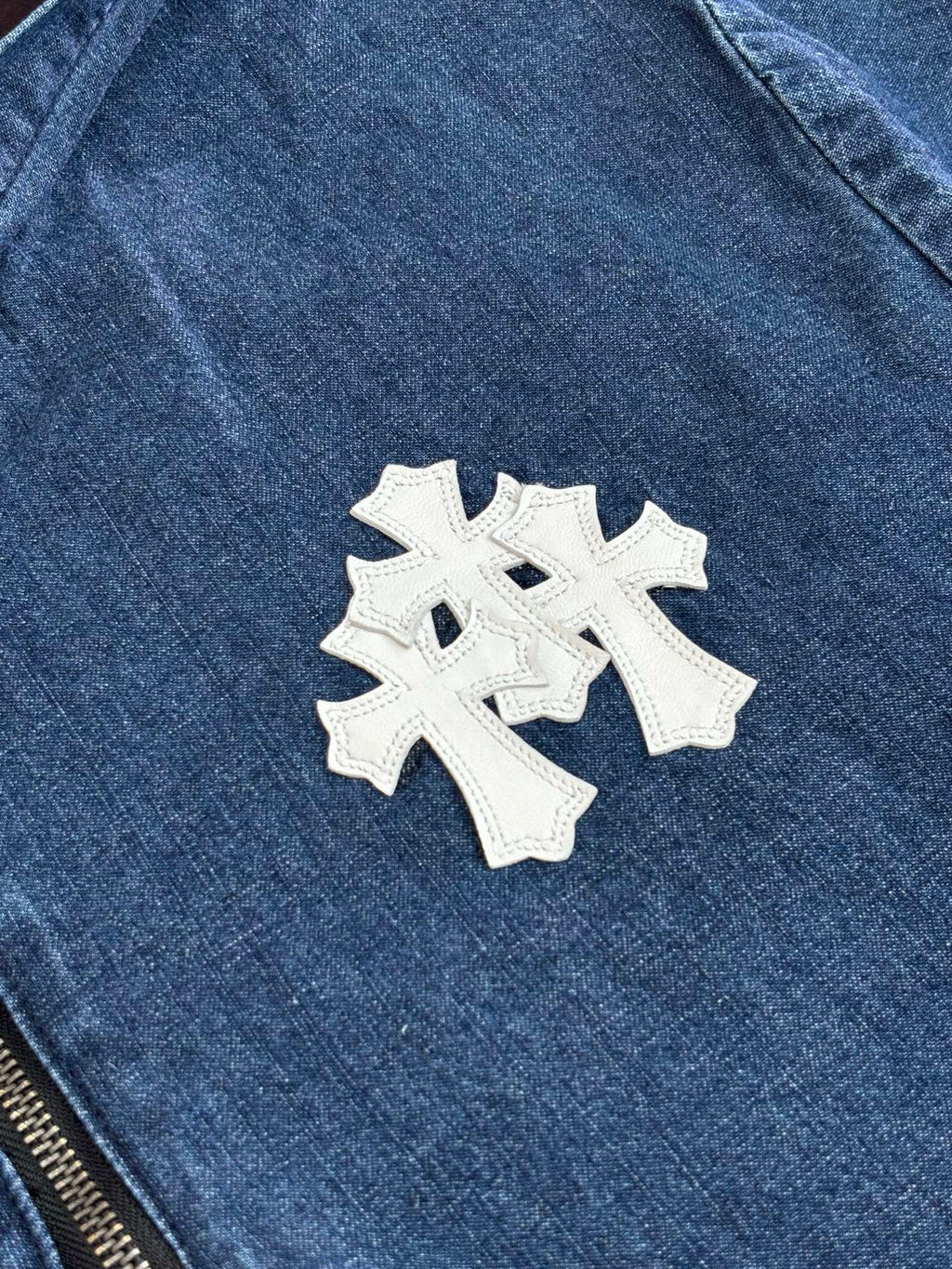 Blue denim jacket close-up with white cross-style embroidered patch on chest.