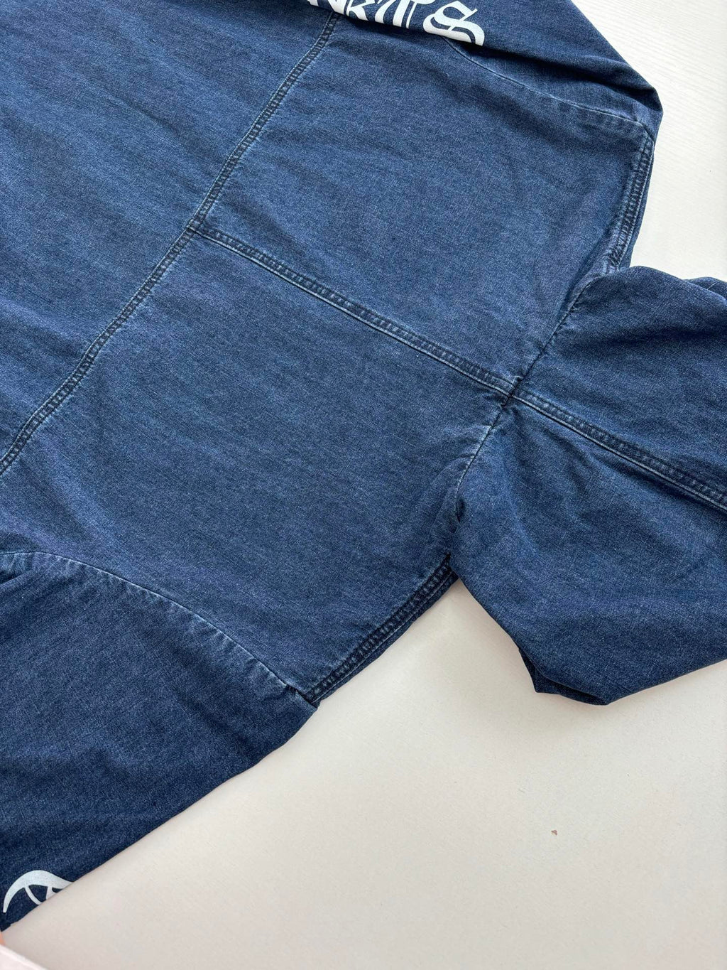 Blue denim hooded jacket close-up with front pocket seams and textured denim finish.