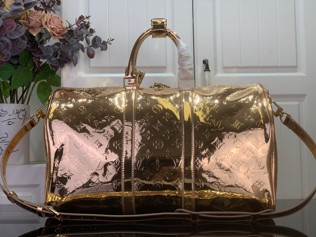 Gold monogram duffel bag with top handles and long shoulder strap, glossy sheen