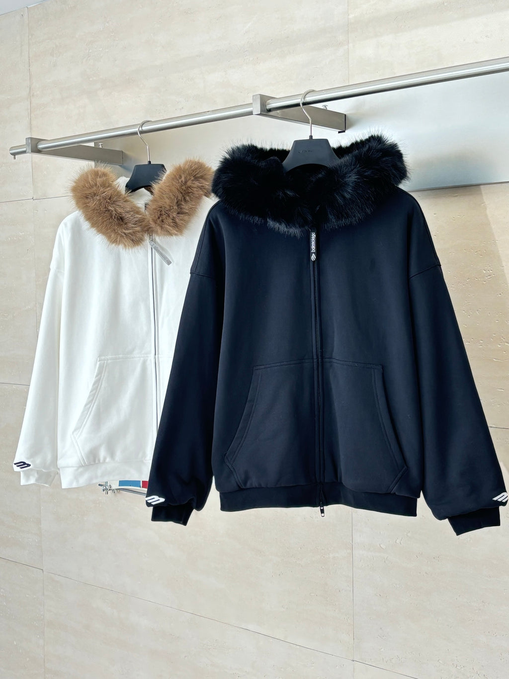 Two hooded zip-up jackets: dark with black fur collar and white with tan fur trim