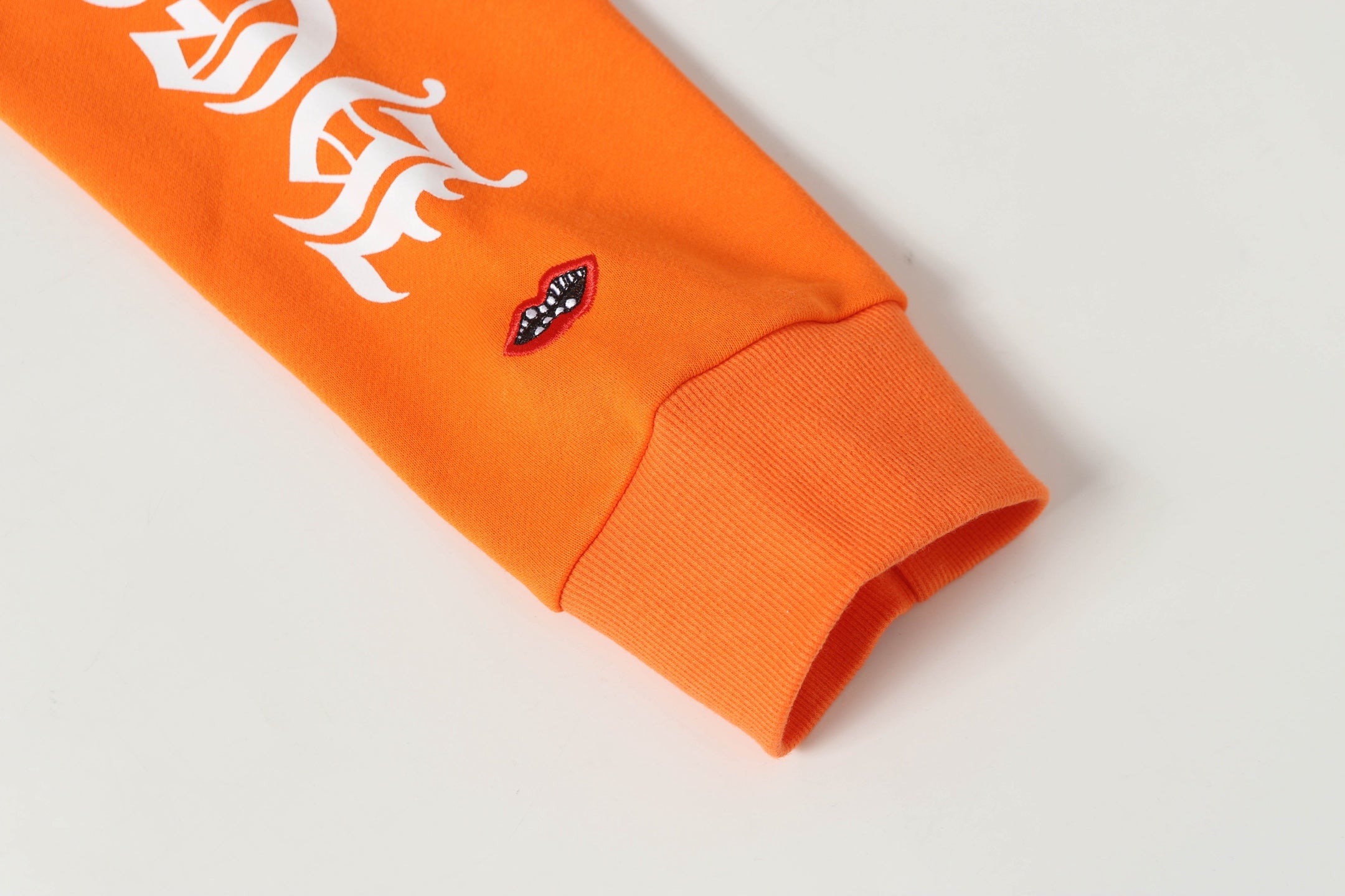 Orange hoodie sleeve cuff with small embroidered logo