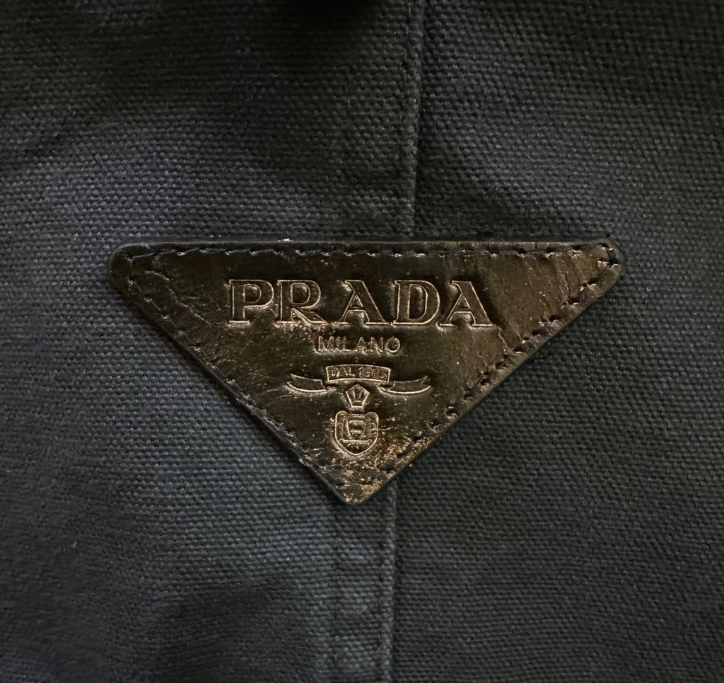 Prada logo patch on dark fabric, triangular emblem with gold lettering