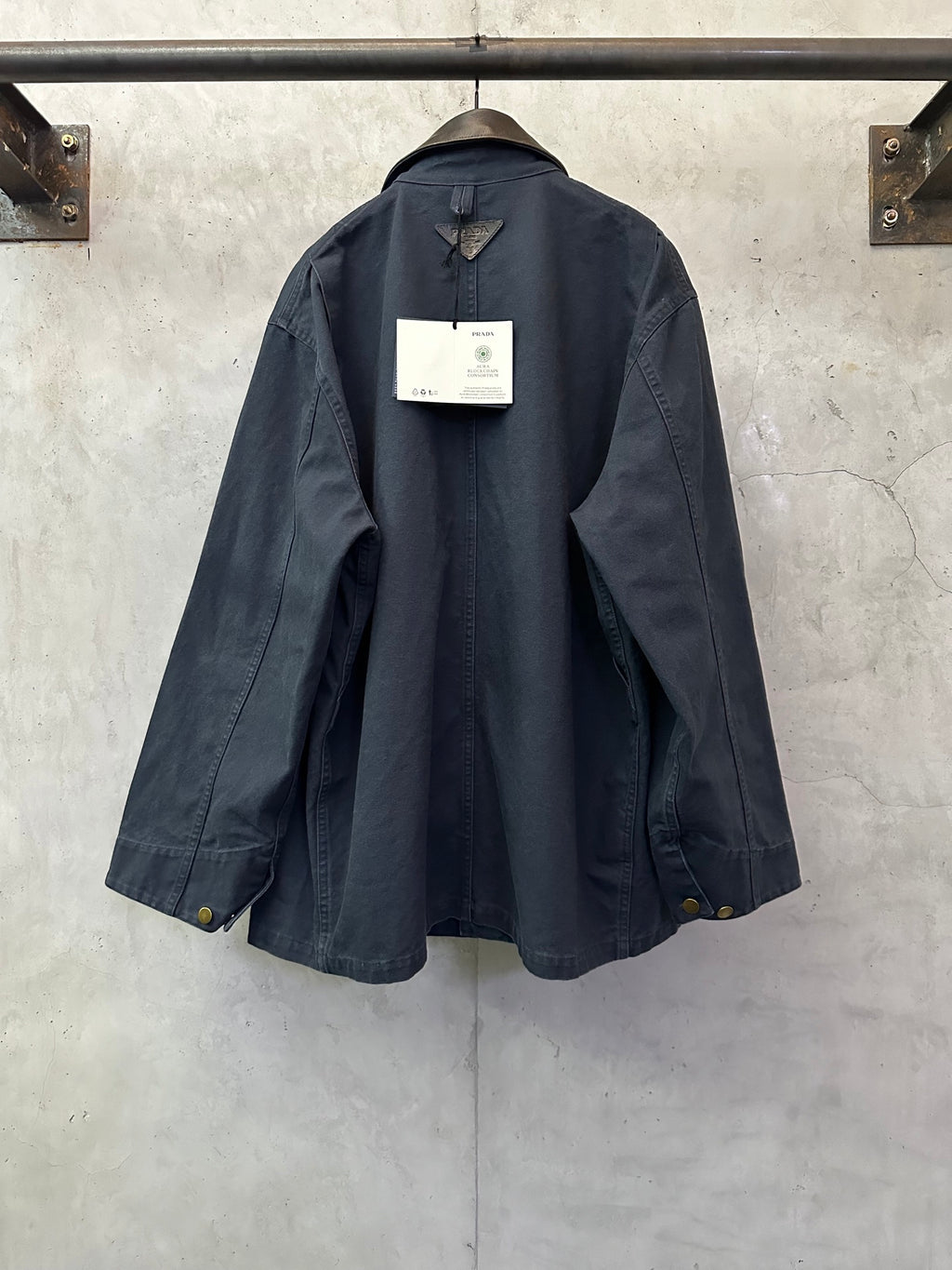 Navy long jacket with curved back hem, side vents, cuff flaps, and back hang tag