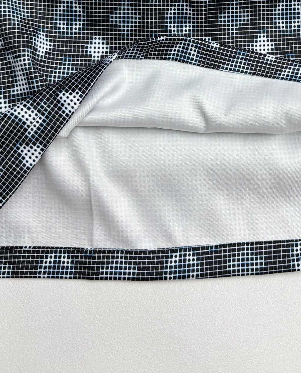Long-sleeve top hem and underside, showing white lining with dark patterned border