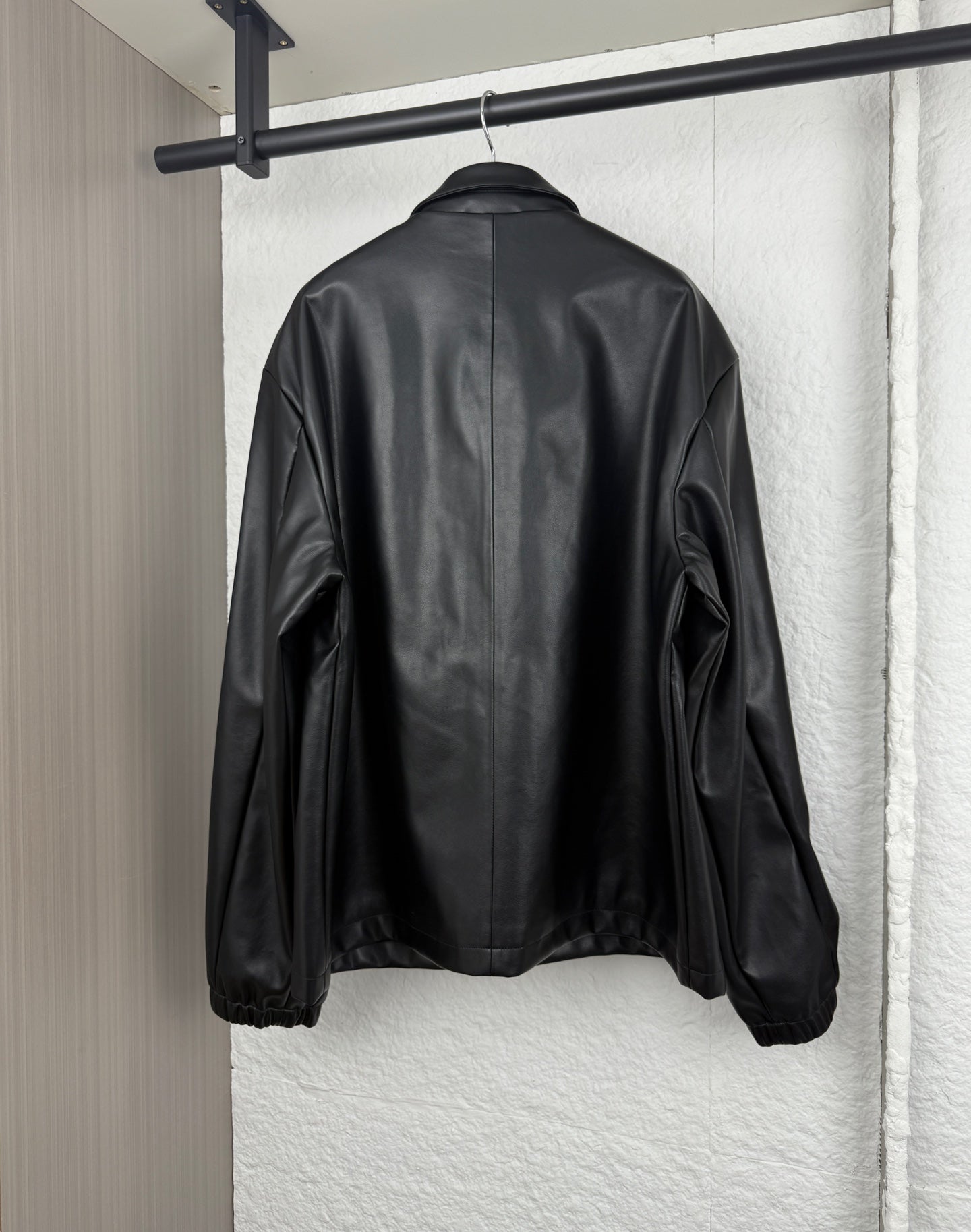 Black leather-look bomber jacket, full back view with snap cuffs