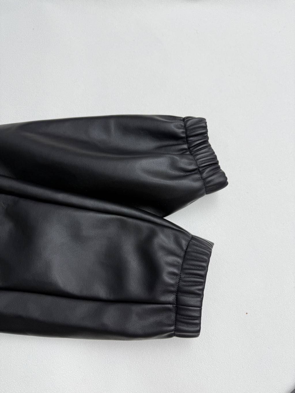 Black leather-look bomber jacket sleeve with gathered ribbed cuff