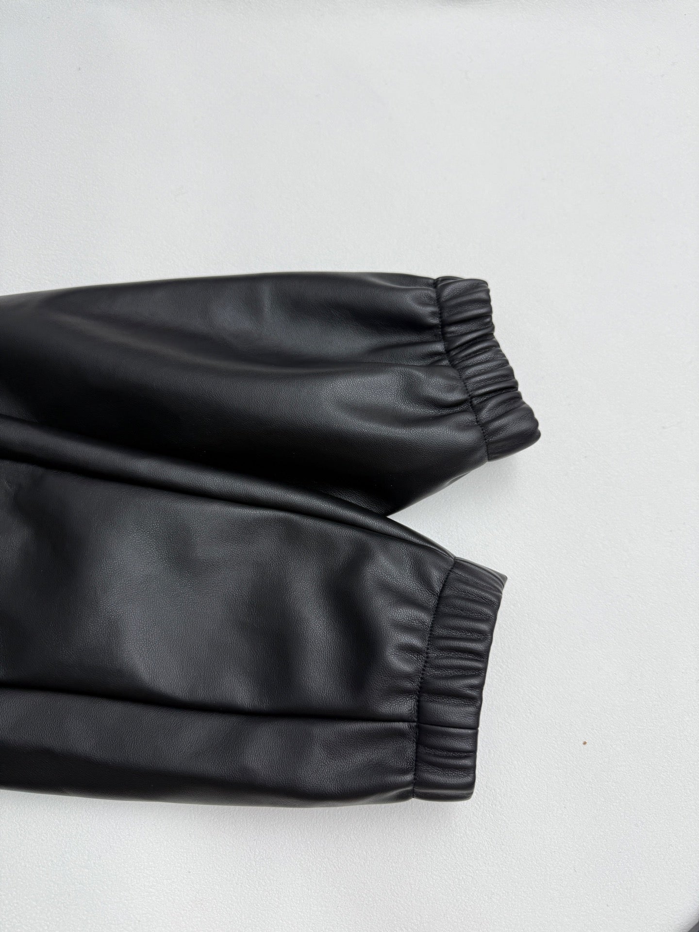Black leather-look bomber jacket sleeve with gathered ribbed cuff