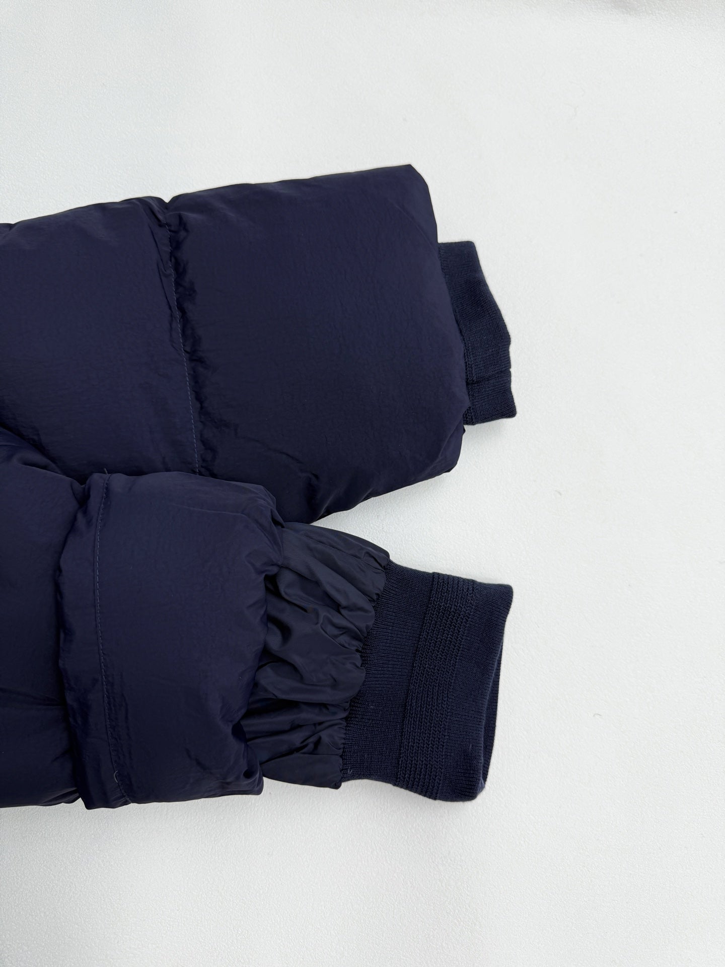 Navy puffer jacket cuffs with elastic ribbing and gathered strap details