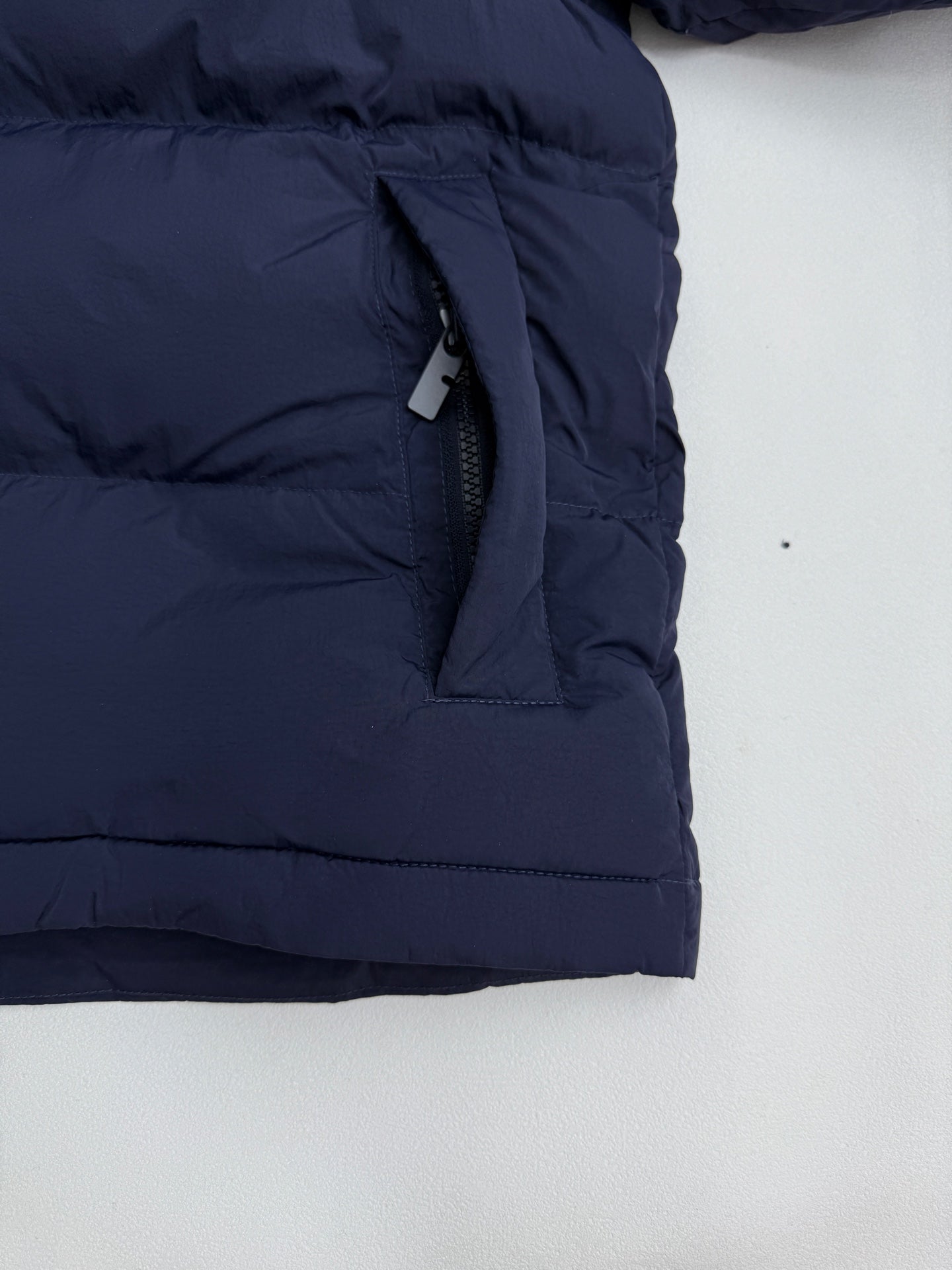 Navy puffer jacket lower front pocket with hanging fabric strap