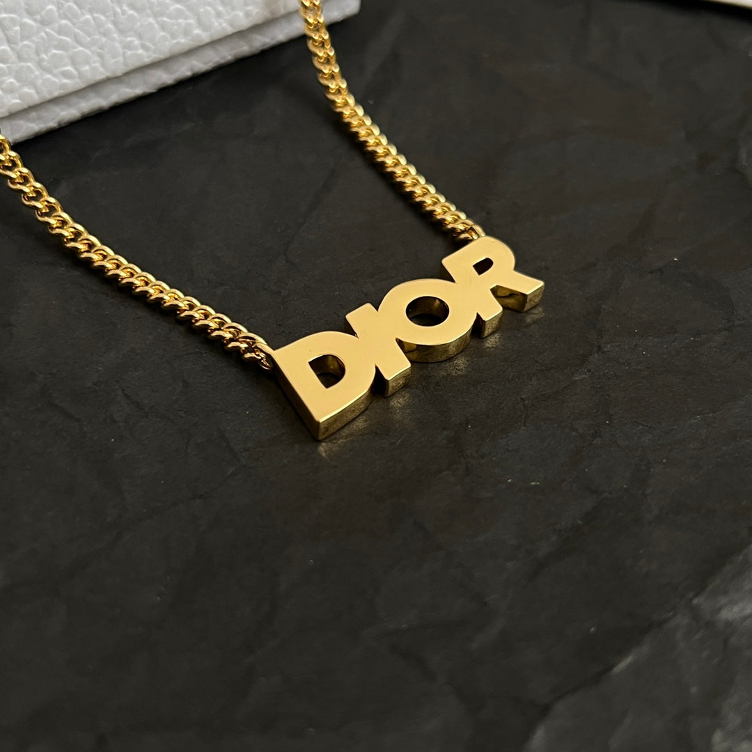 Close-up of gold-tone Dior pendant on curb chain necklace.