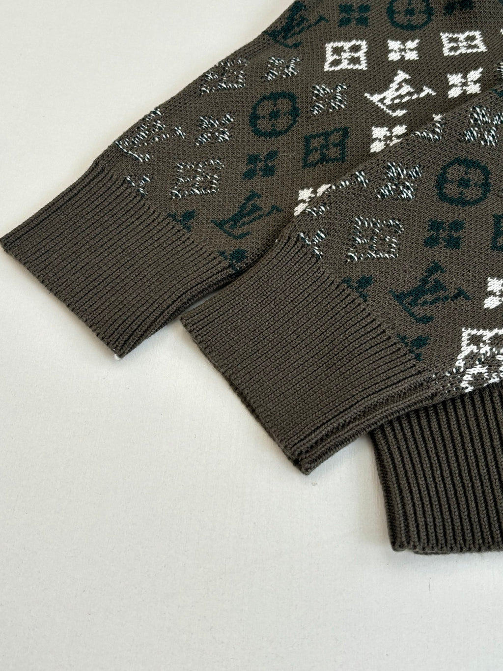 Knit sweater cuff and hem detail in dark tone with allover logo-style pattern