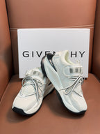 White sneakers close-up with logo straps, gray laces, and dark rubber outsole