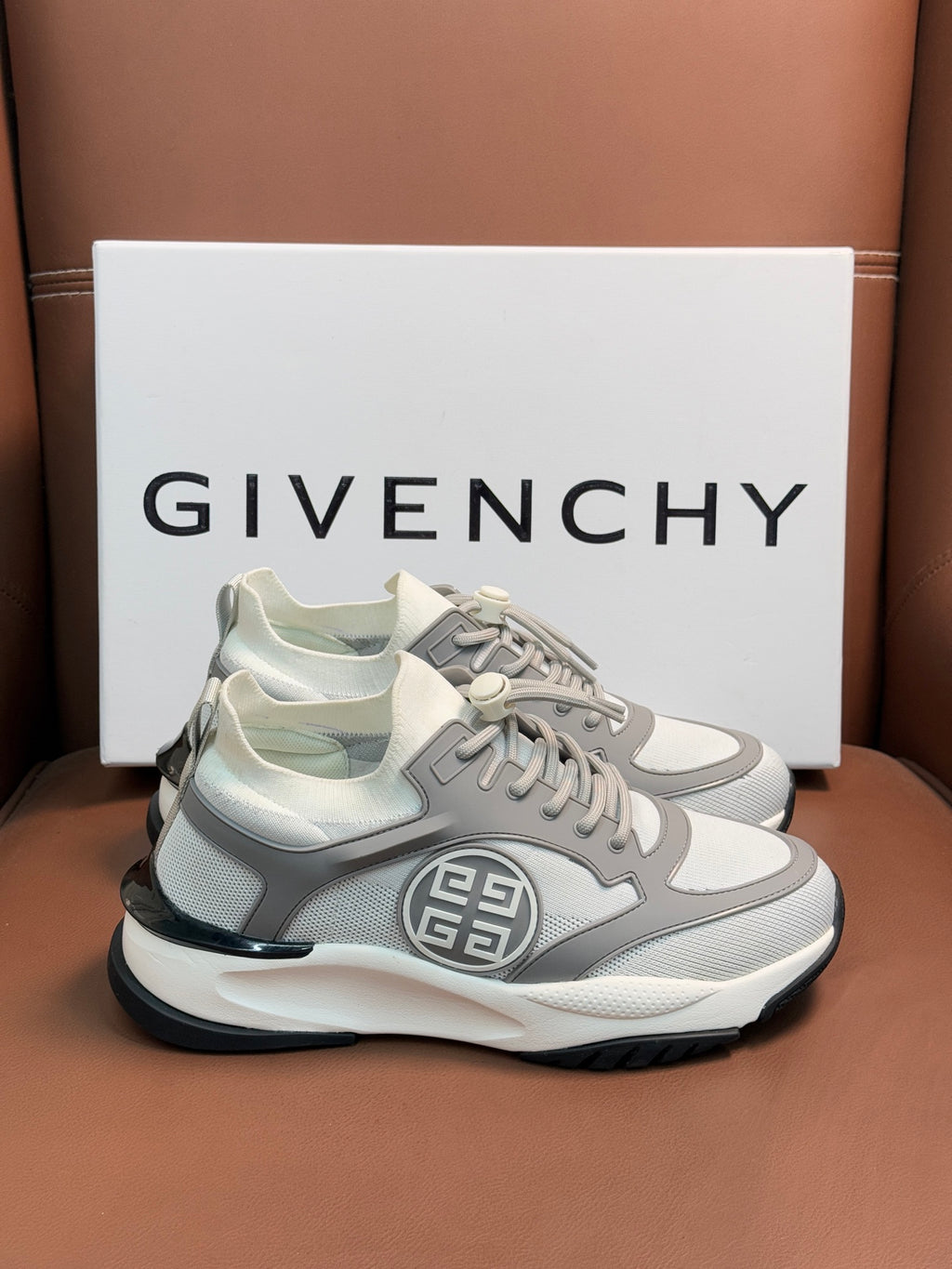 Light gray chunky sneakers with dark trim, lace closure, and front logo emblem.