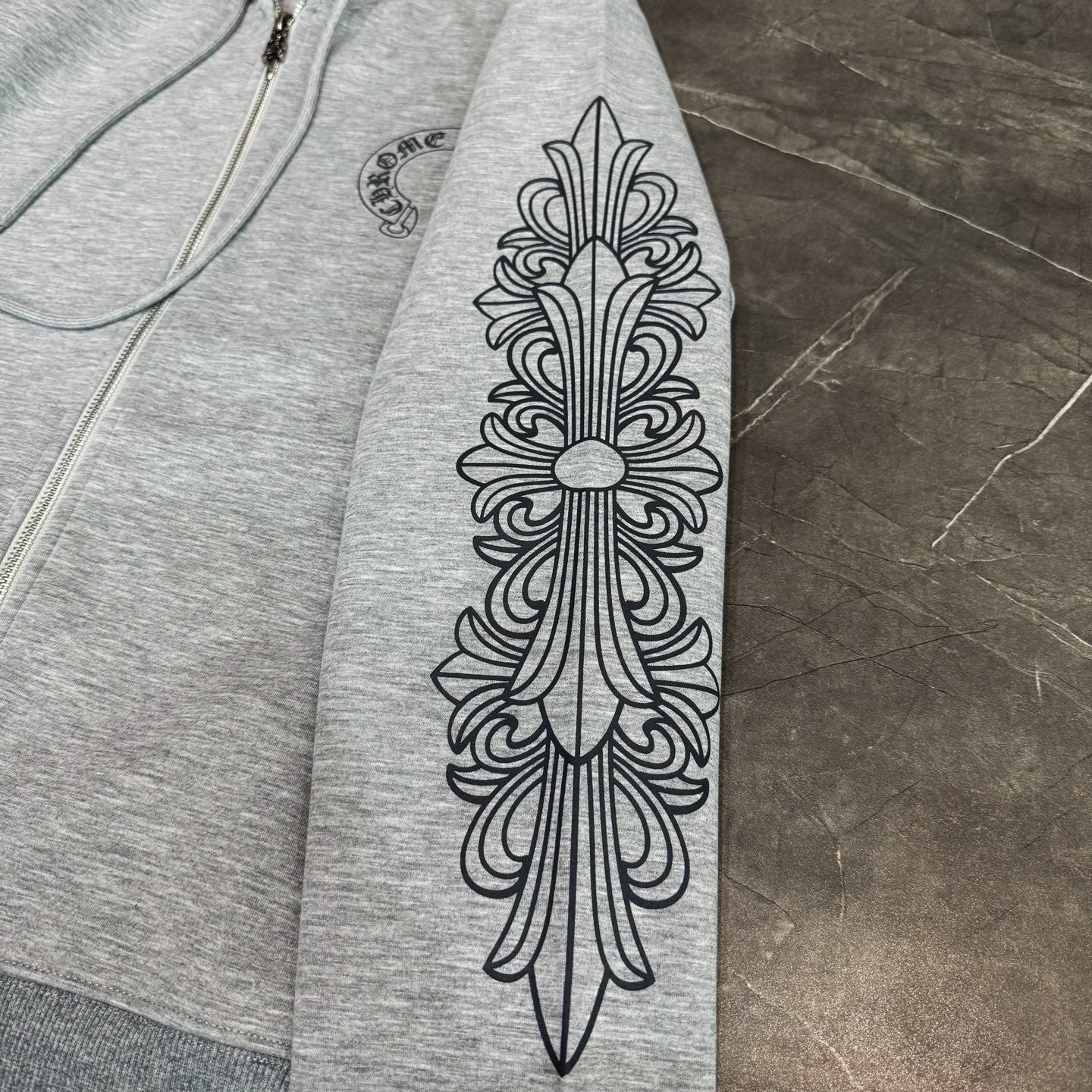 Grey hoodie sleeve with ornate leaf-like emblem graphic print