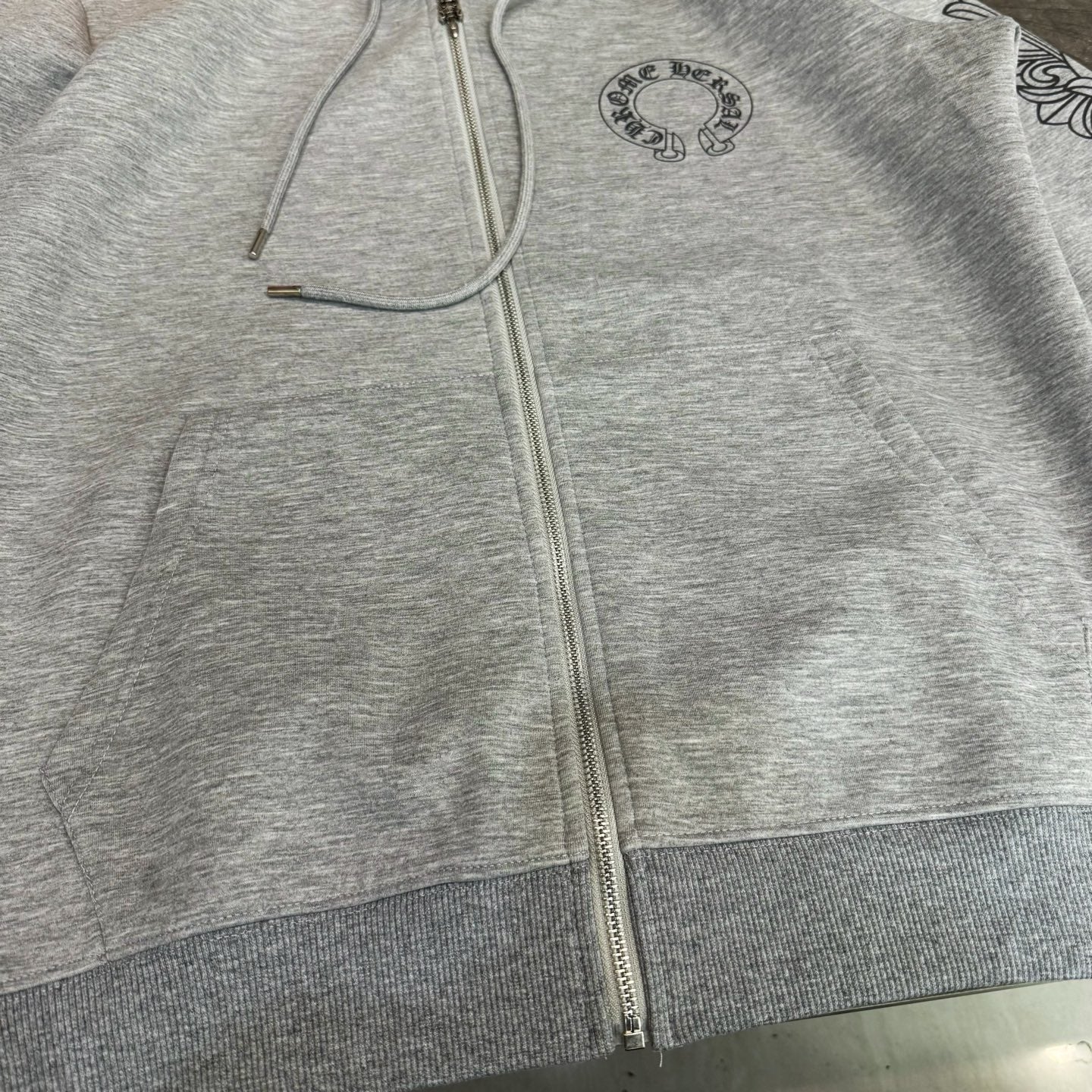 Grey zip-up hoodie front close-up with drawstrings and zipper