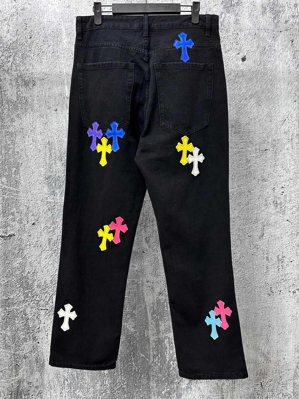 Black denim pants with scattered colorful cross patches, front and back view