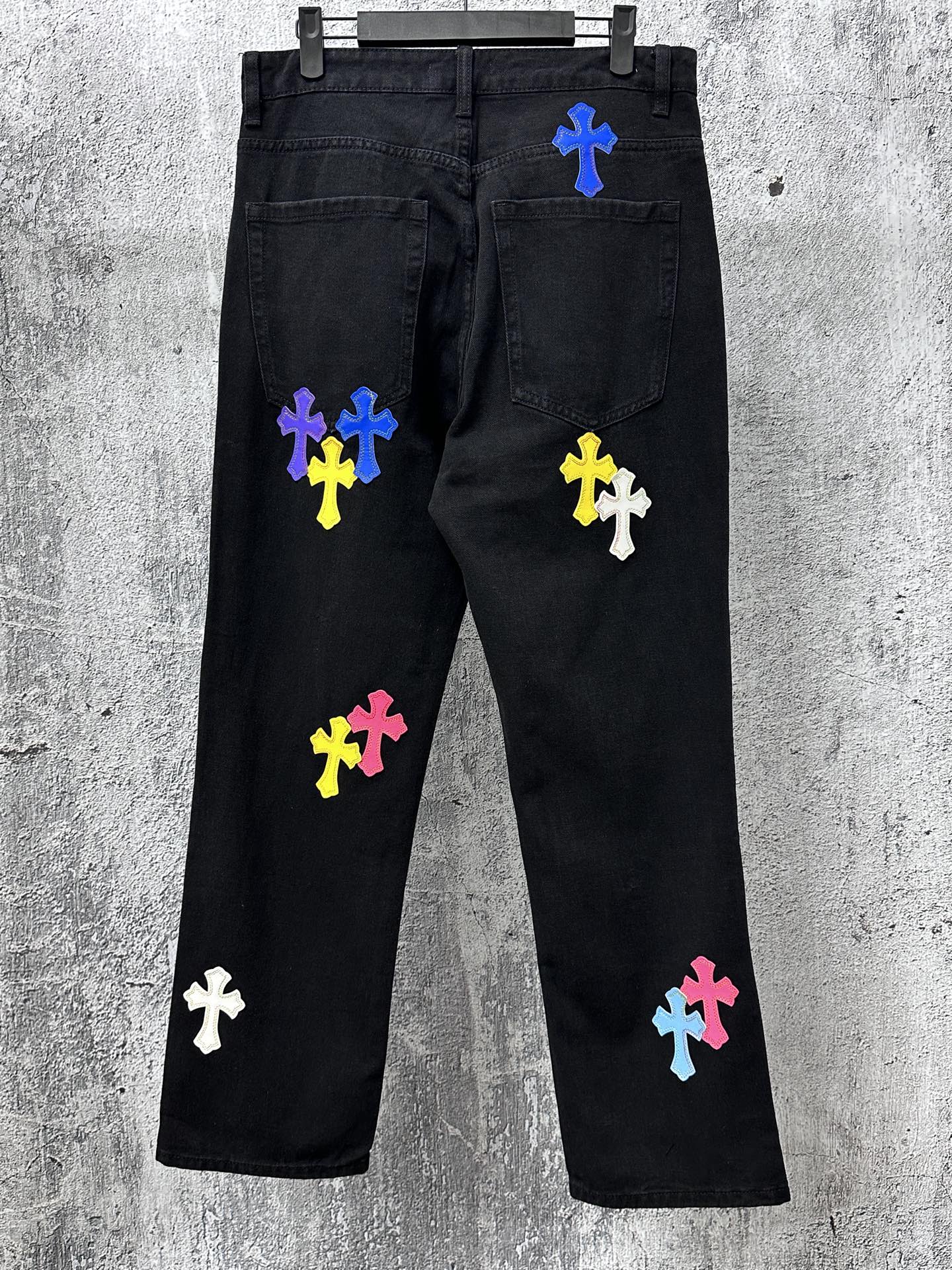 Black denim pants with scattered colorful cross patches, front and back view