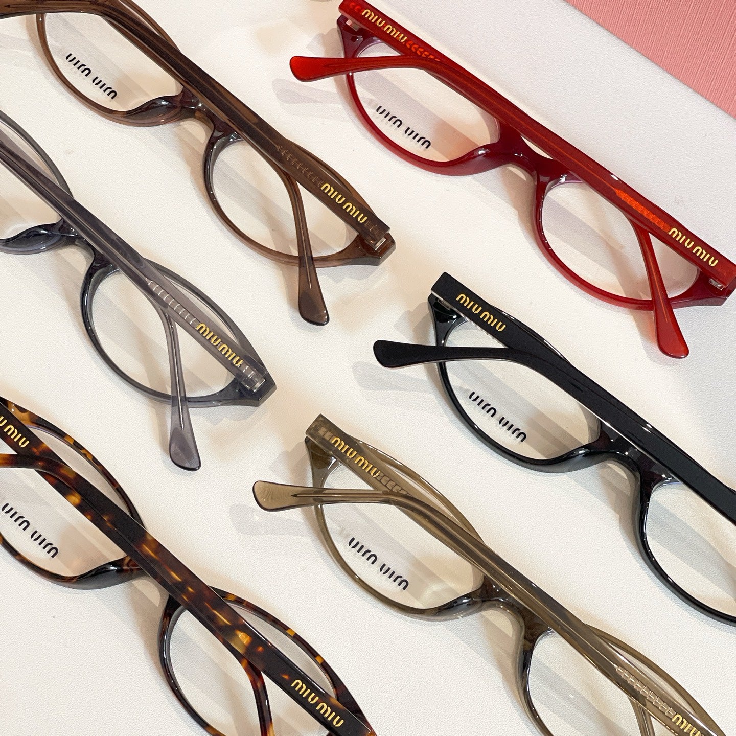 Assorted Miu Miu eyeglasses with dark, red, and tortoise frames arranged together
