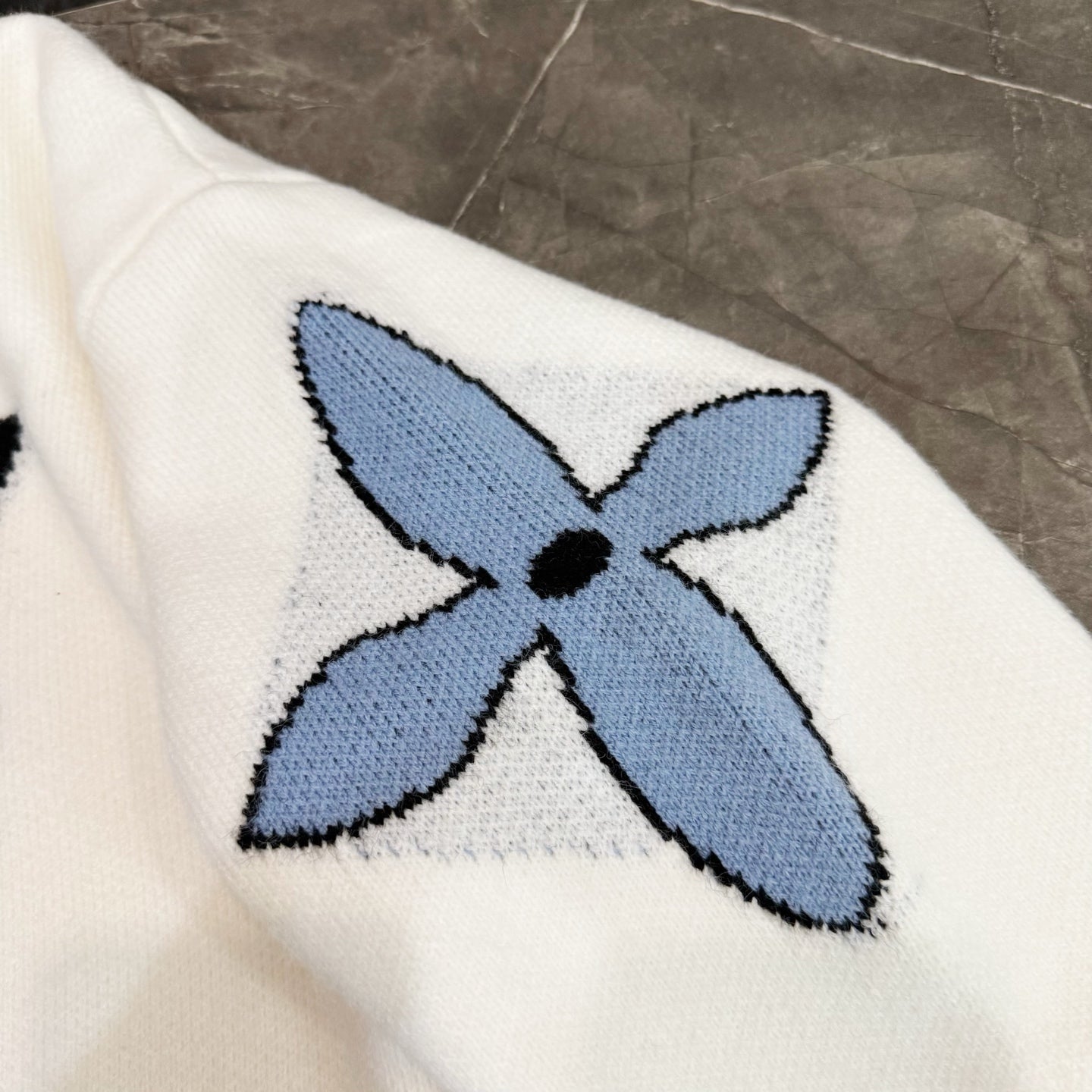 White knit sweater with blue flower applique and black center, crew neck