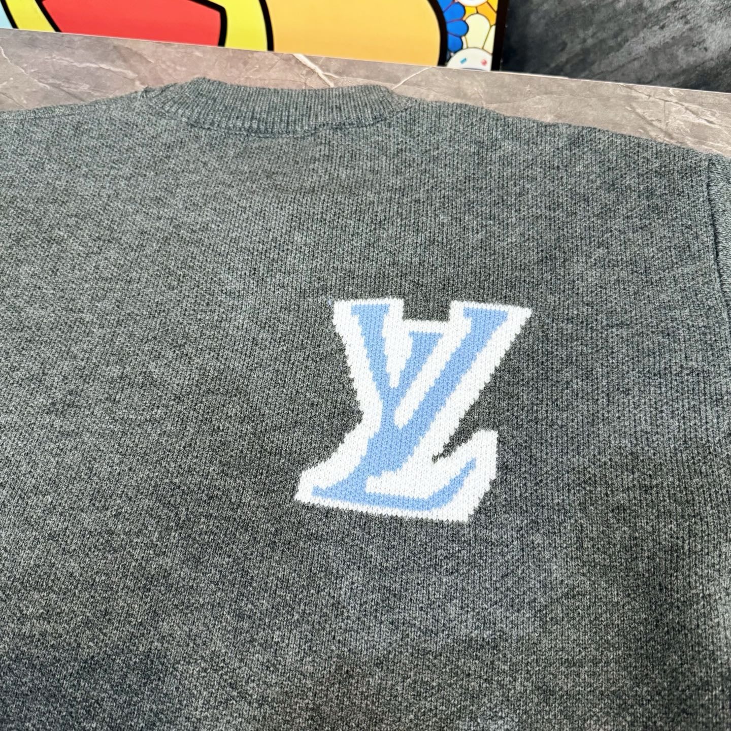 Gray knit long-sleeve sweater with blue LV-style logo centered on the back