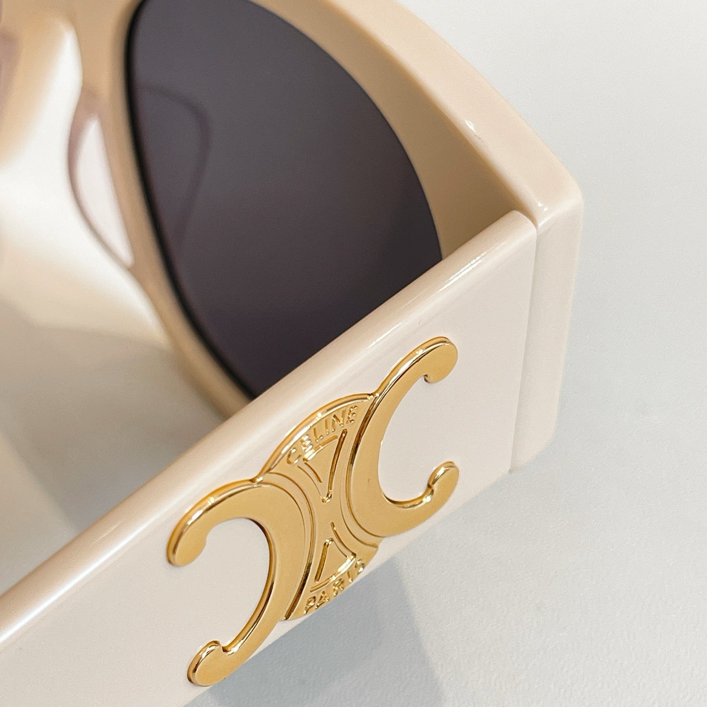 Celine sunglasses close-up: gold emblem on cream frame with dark lens
