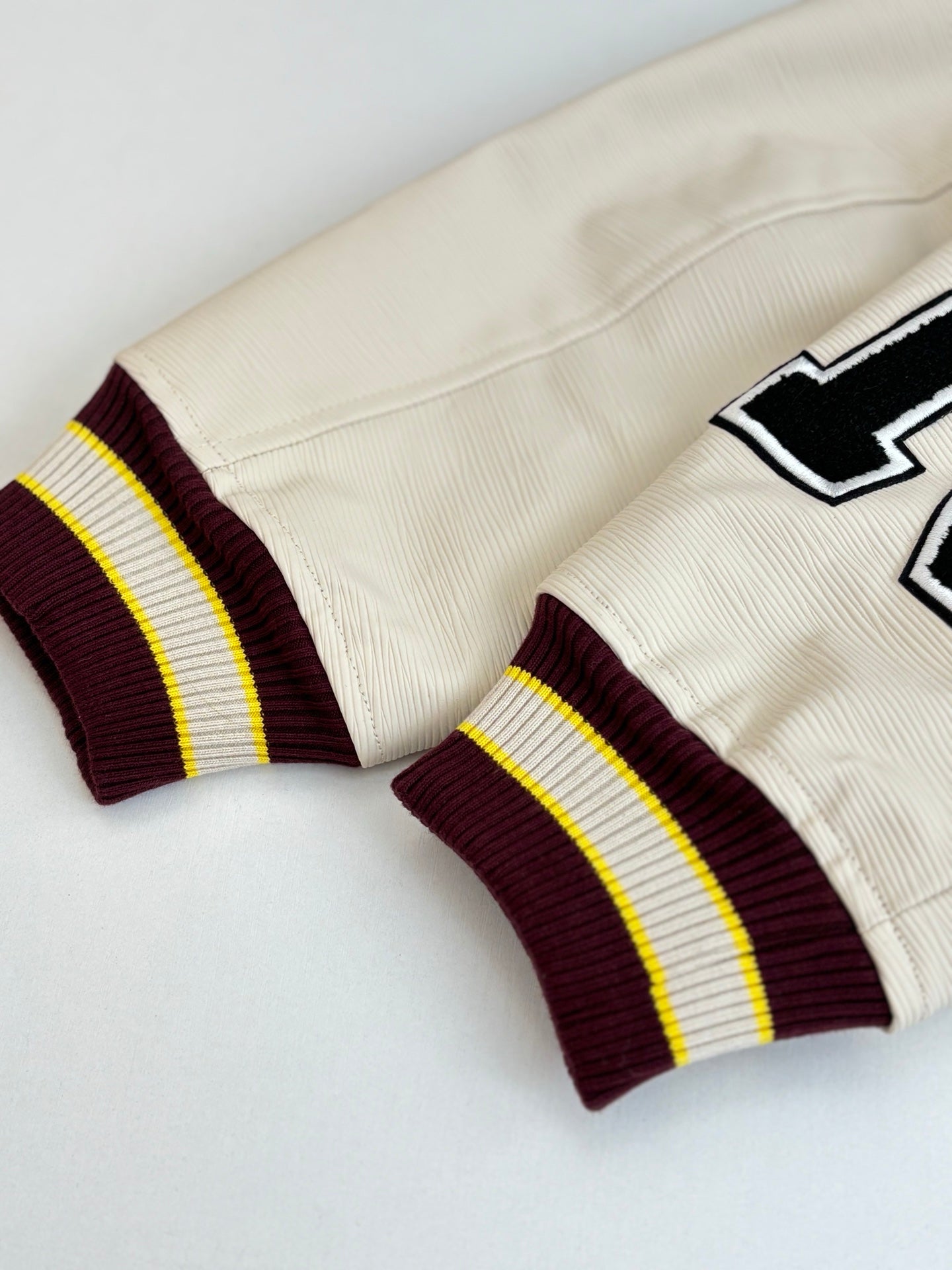 Cream long pants with striped maroon-and-yellow knit cuffs and LV chevron patch