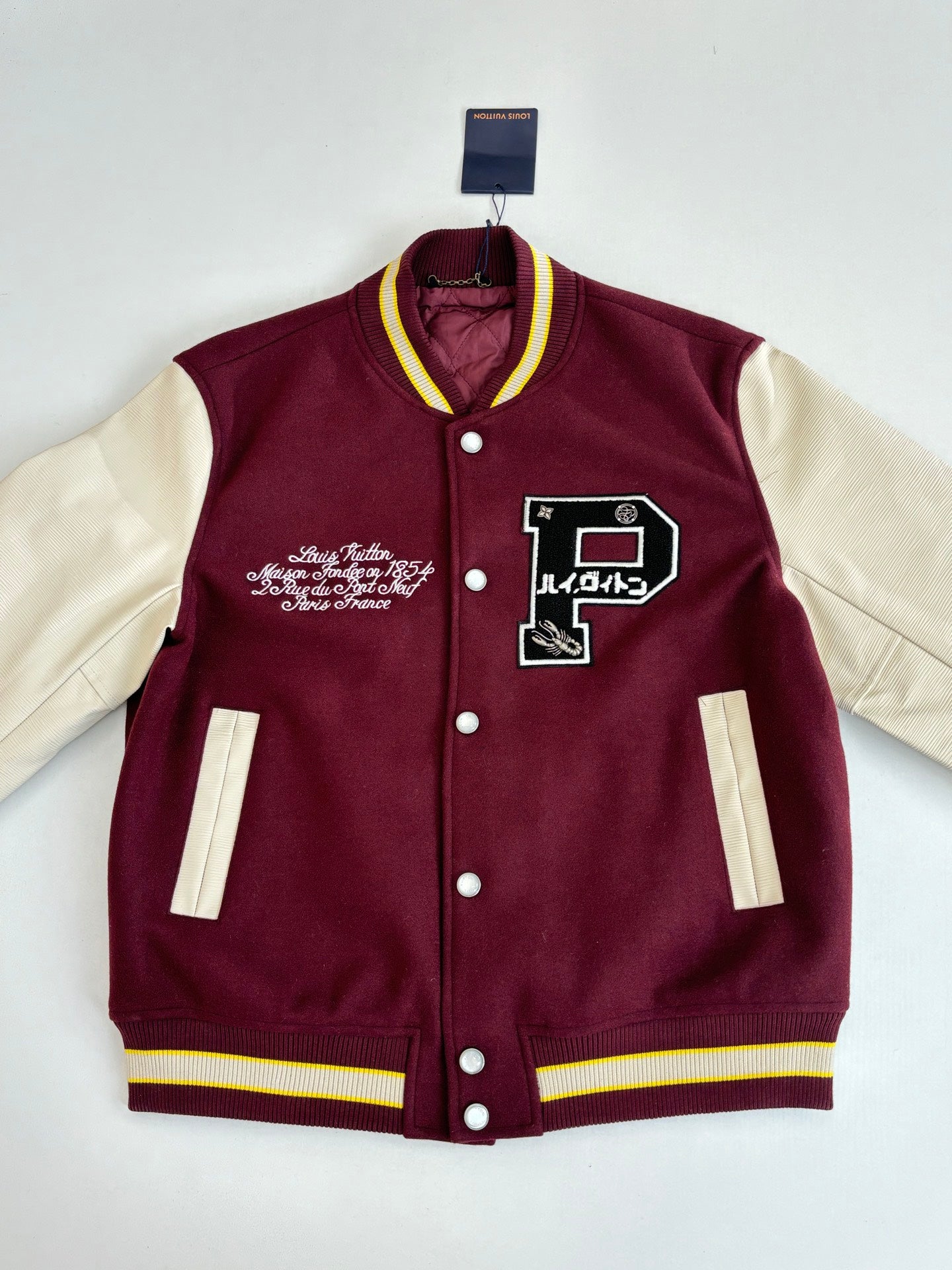 Maroon varsity jacket with white sleeves, front patches, striped ribbed cuffs, snap buttons.