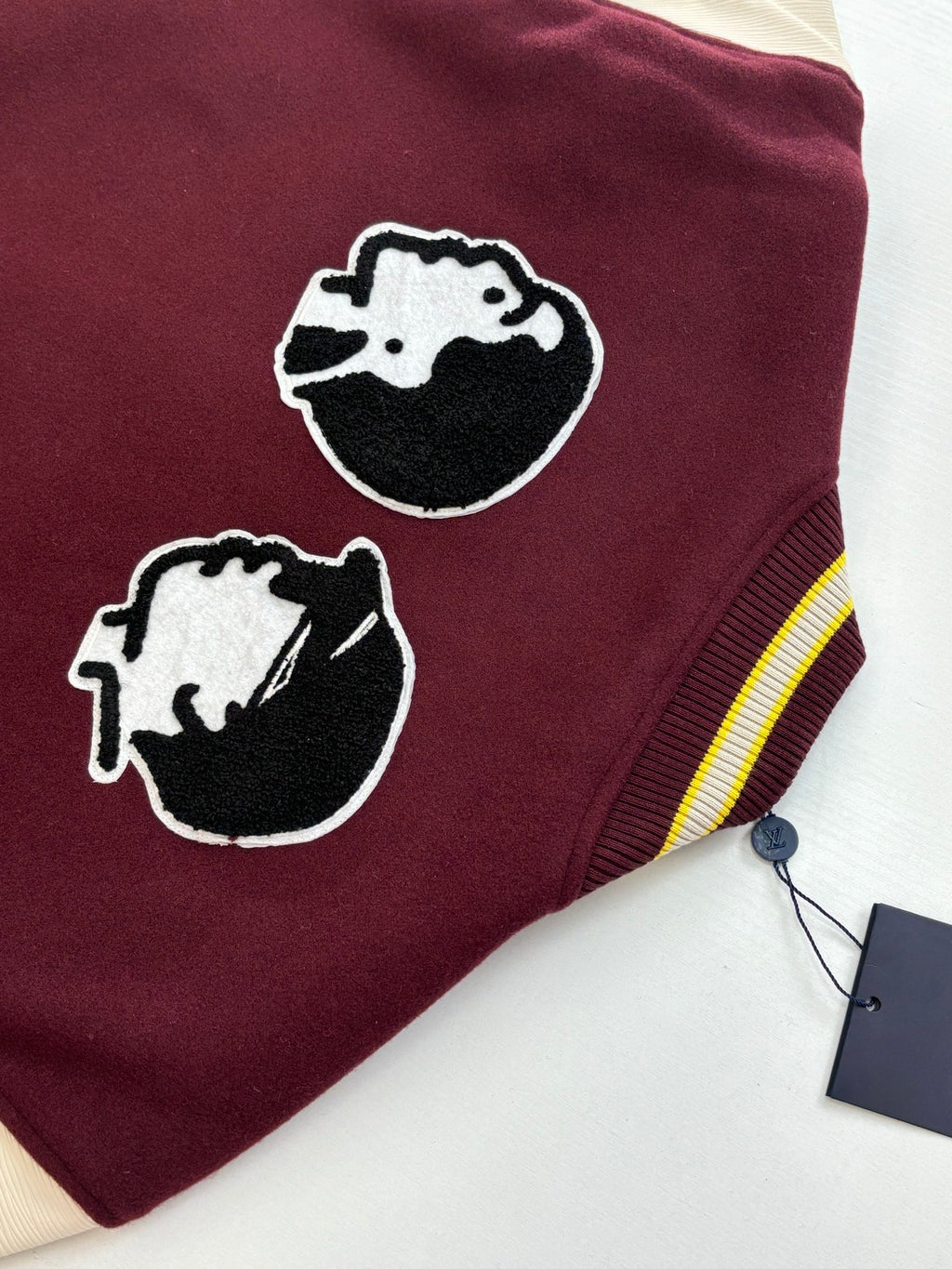 Maroon varsity jacket close-up with two dog-head patches and striped cuff ribbing.